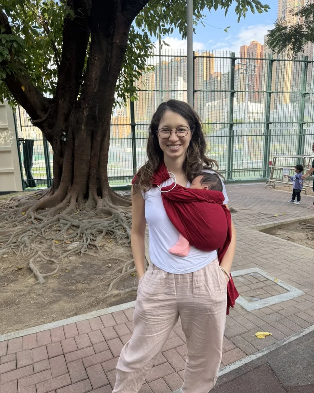 Alexandra Colgan carrying her newborn in a red ring sling, outdoors in Hong Kong.
